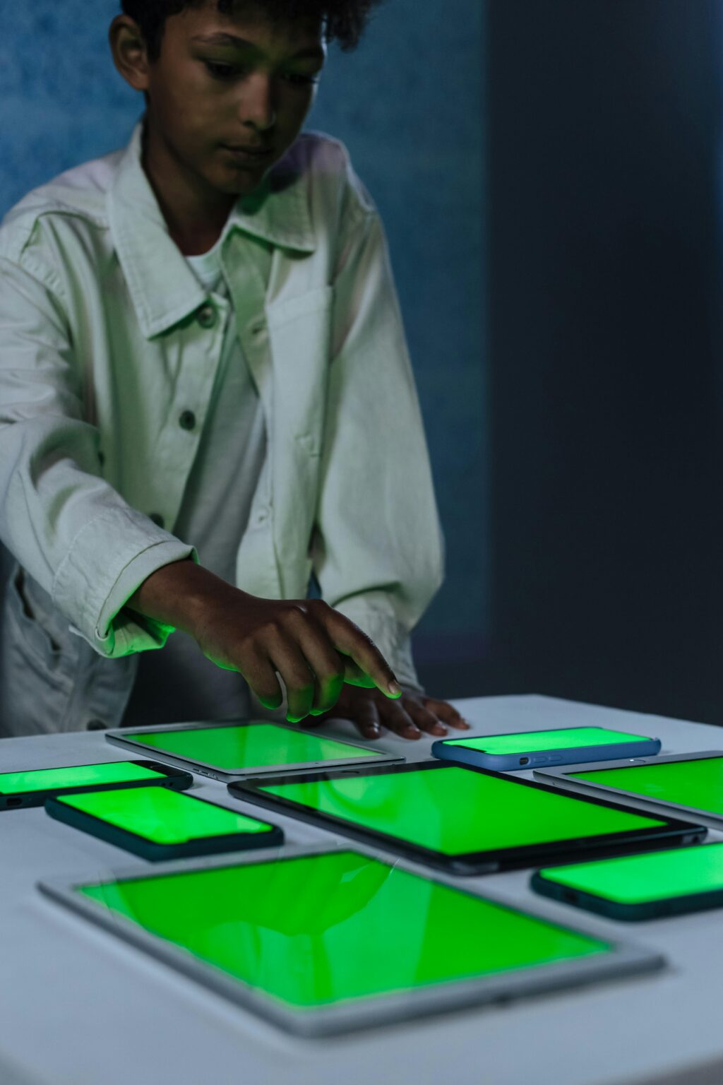 A teenager interacts with multiple green screen tablets for digital exploration.