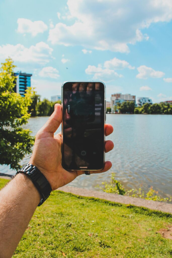 Person holding a smartphone by a scenic lake with city skyline in Cluj-Napoca, Romania.